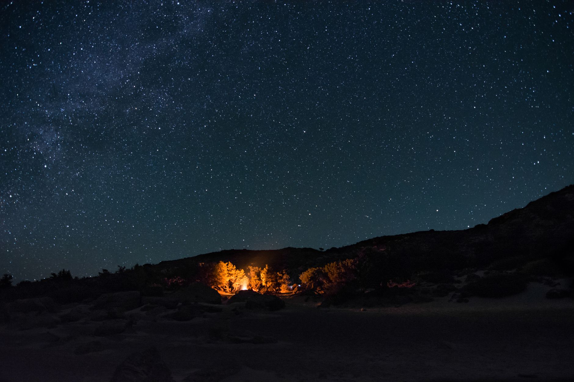 Illustrative photograph: a small fire glowing among desert shrubs beneath a starfield