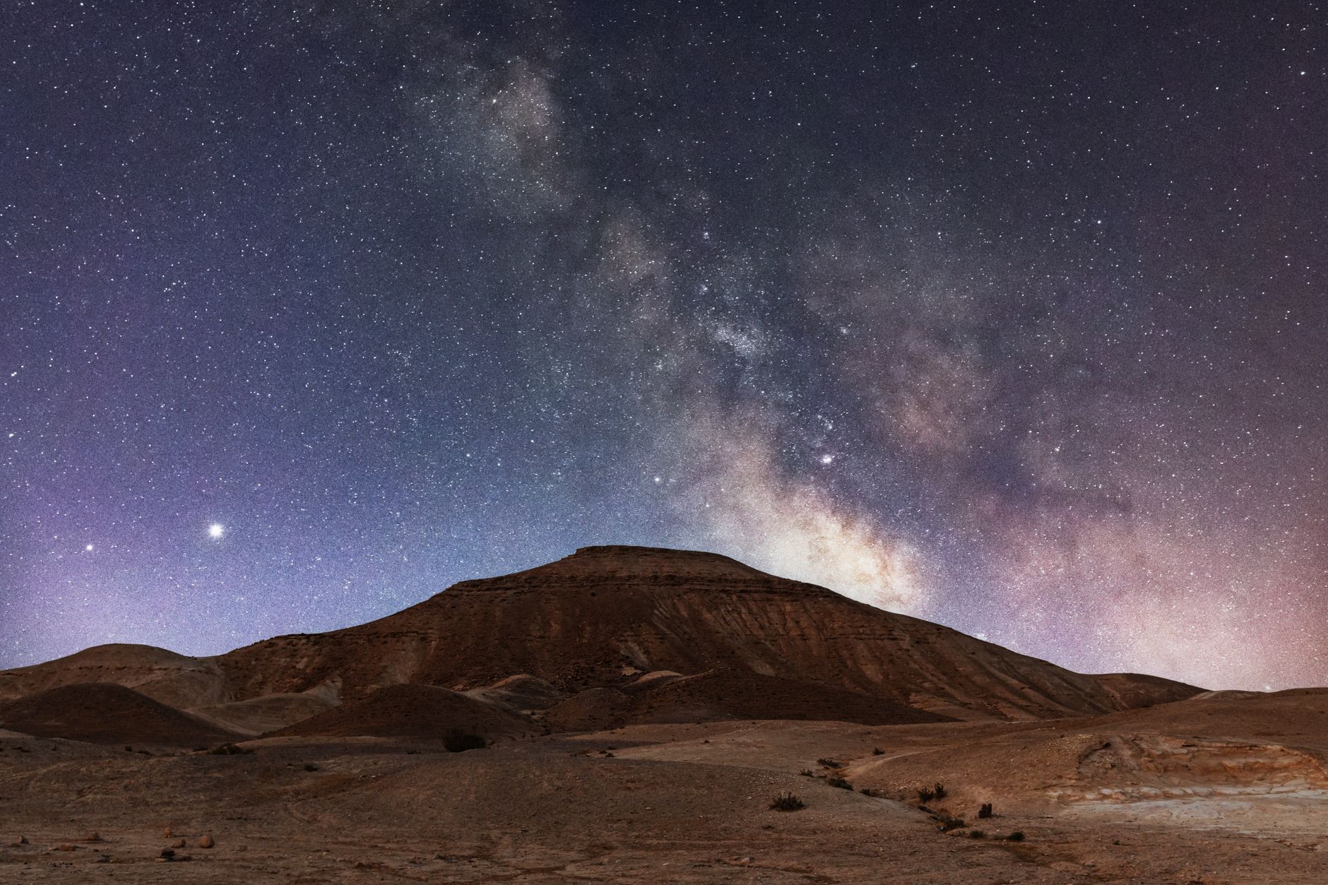 Illustrative photograph: the Milky Way rising over a bare desert hill at night