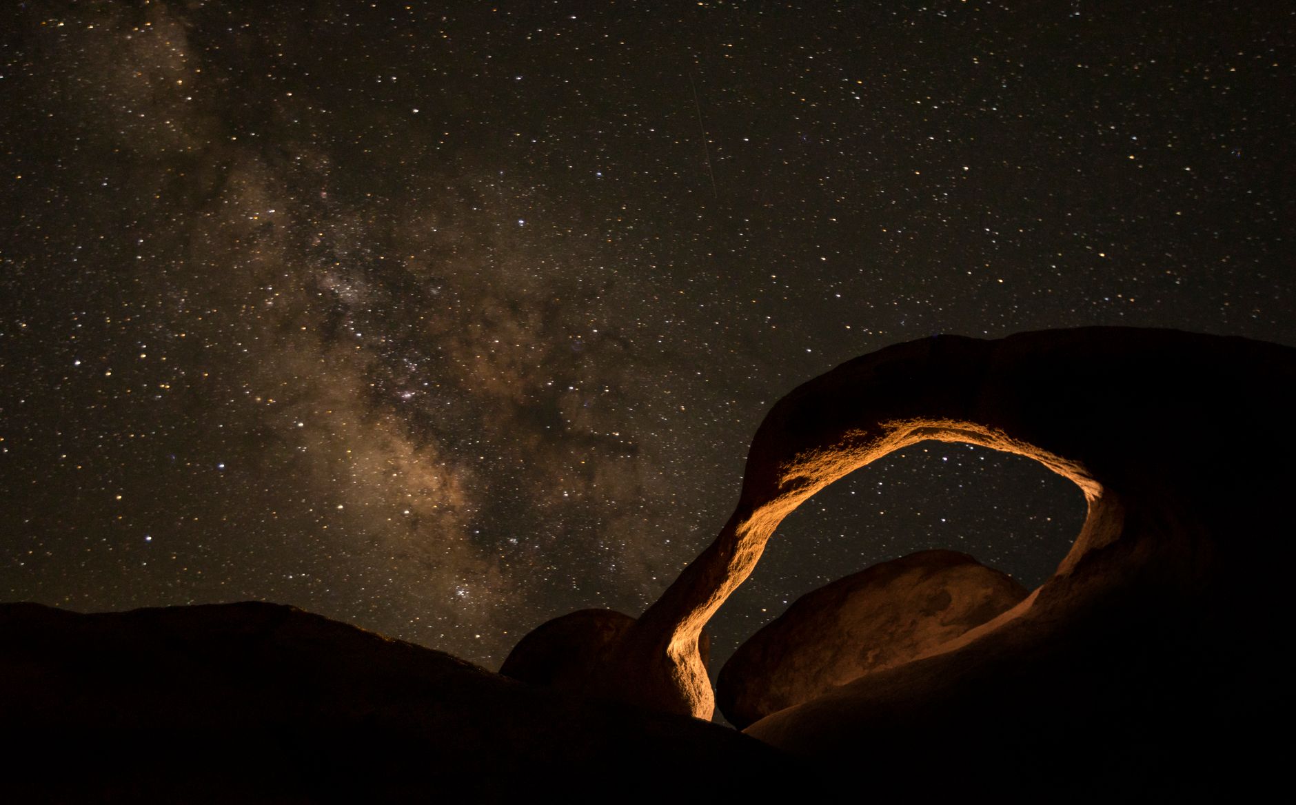 Illustrative photograph: a rock arch lit warm orange under a starry sky